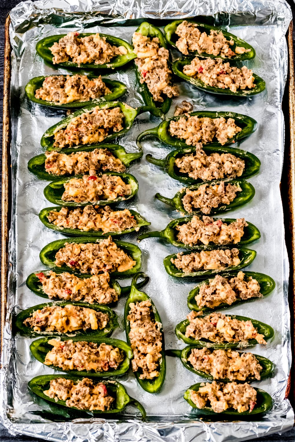 uncooked stuffed jalapeño peppers on a foil-lined baking sheet