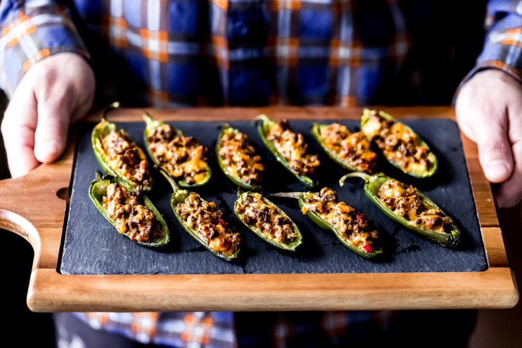 a man holding a cutting board with venison stuffed jalapeño peppers on it
