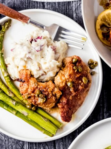 a plate of pheasant piccata, mashed potatoes, and asparagus