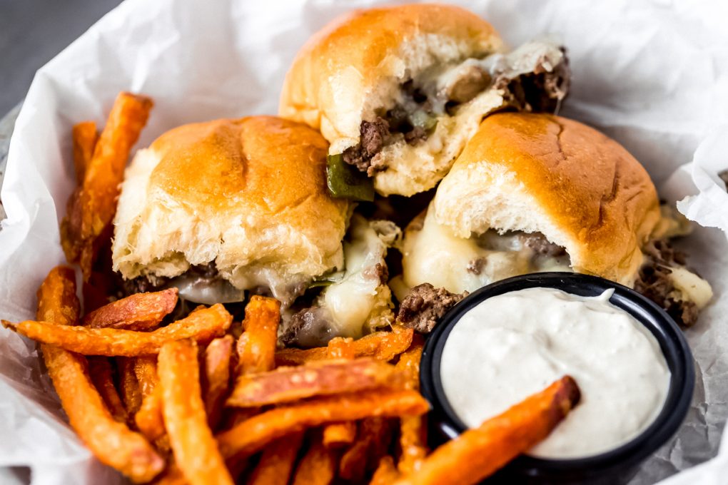 a platter of three venison philly cheesesteak sliders served with sweet potato fries and a dipping sauce