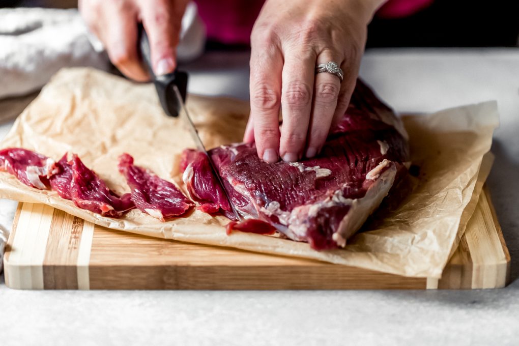 a woman thinly slicing an elk tri-tip roast