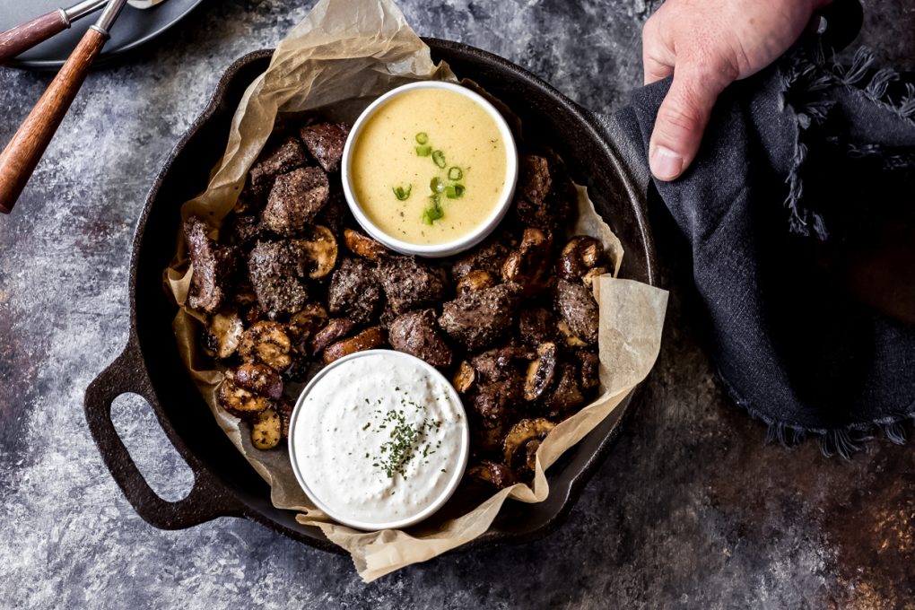 a man holding a cast iron skillet with air fryer venison steak bites and mushrooms