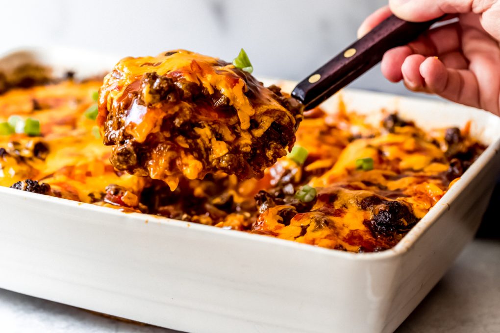 a person dishing out a serving from a ground venison enchilada casserole
