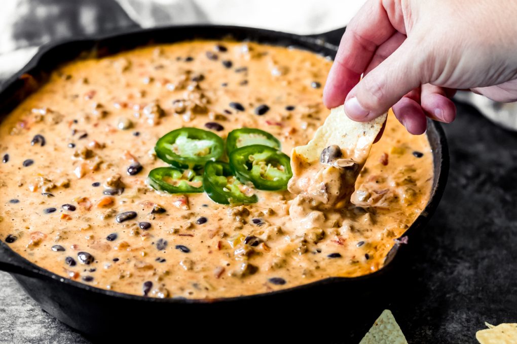 a woman dipping a tortilla chip into loaded venison queso dip