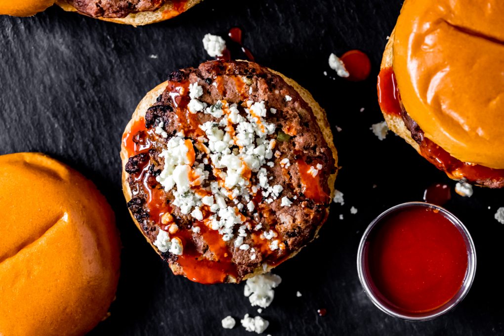 a spicy buffalo bison burger on a bun with blue cheese crumbles and buffalo sauce