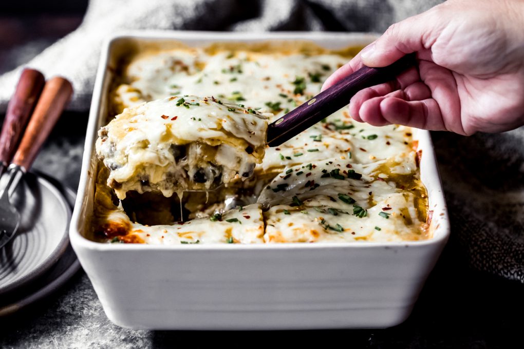 a woman pulling out a serving of ground venison green chile enchilada casserole 