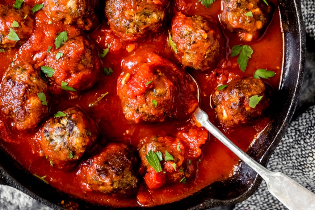 a skillet of ground venison meatballs in marinara sauce with a spoon in the skillet
