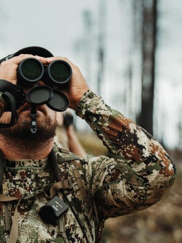 a man hunting looking through binoculars