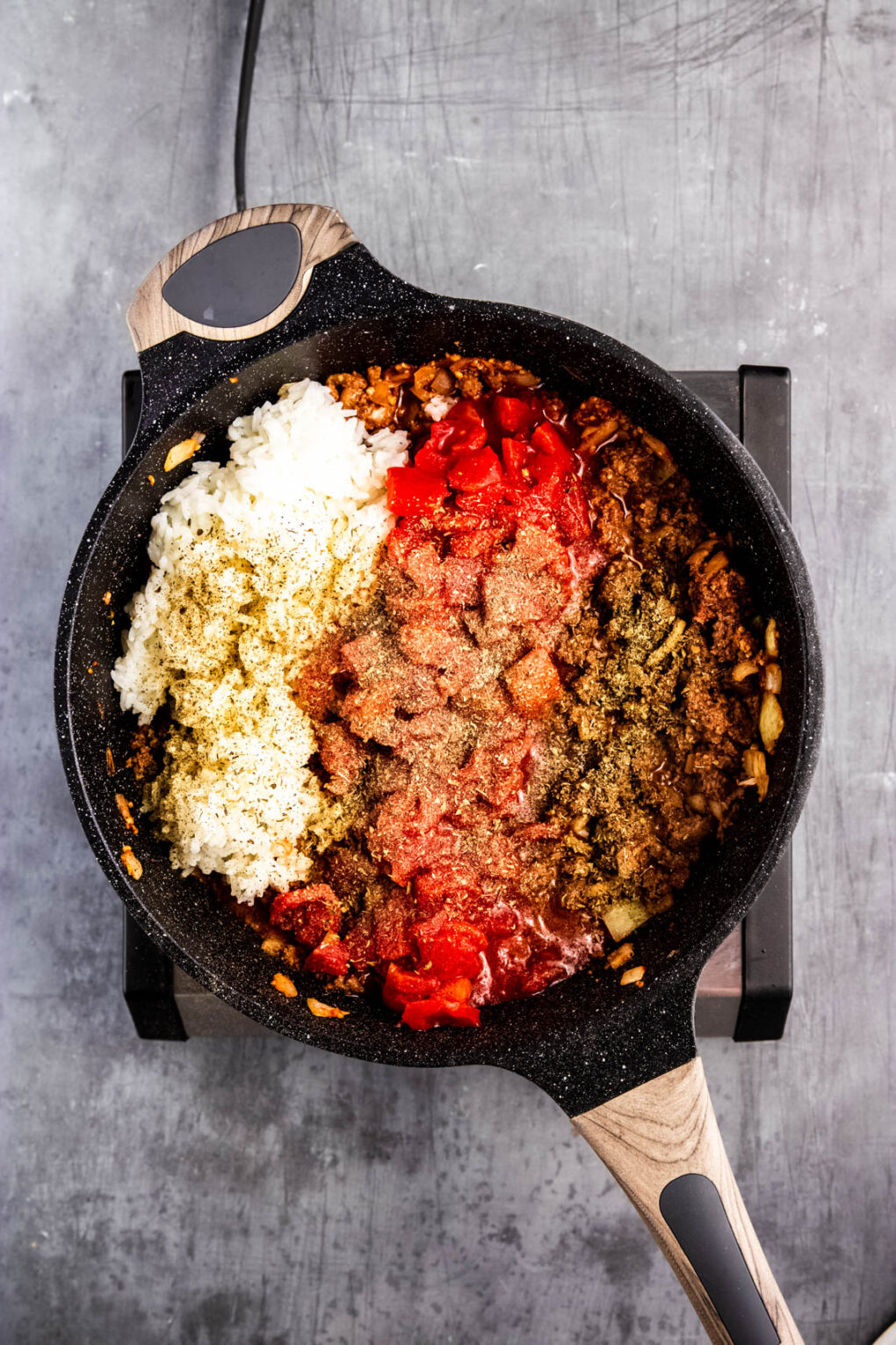 Meat separated with the tomatoes, seasonings, and rice in a skillet